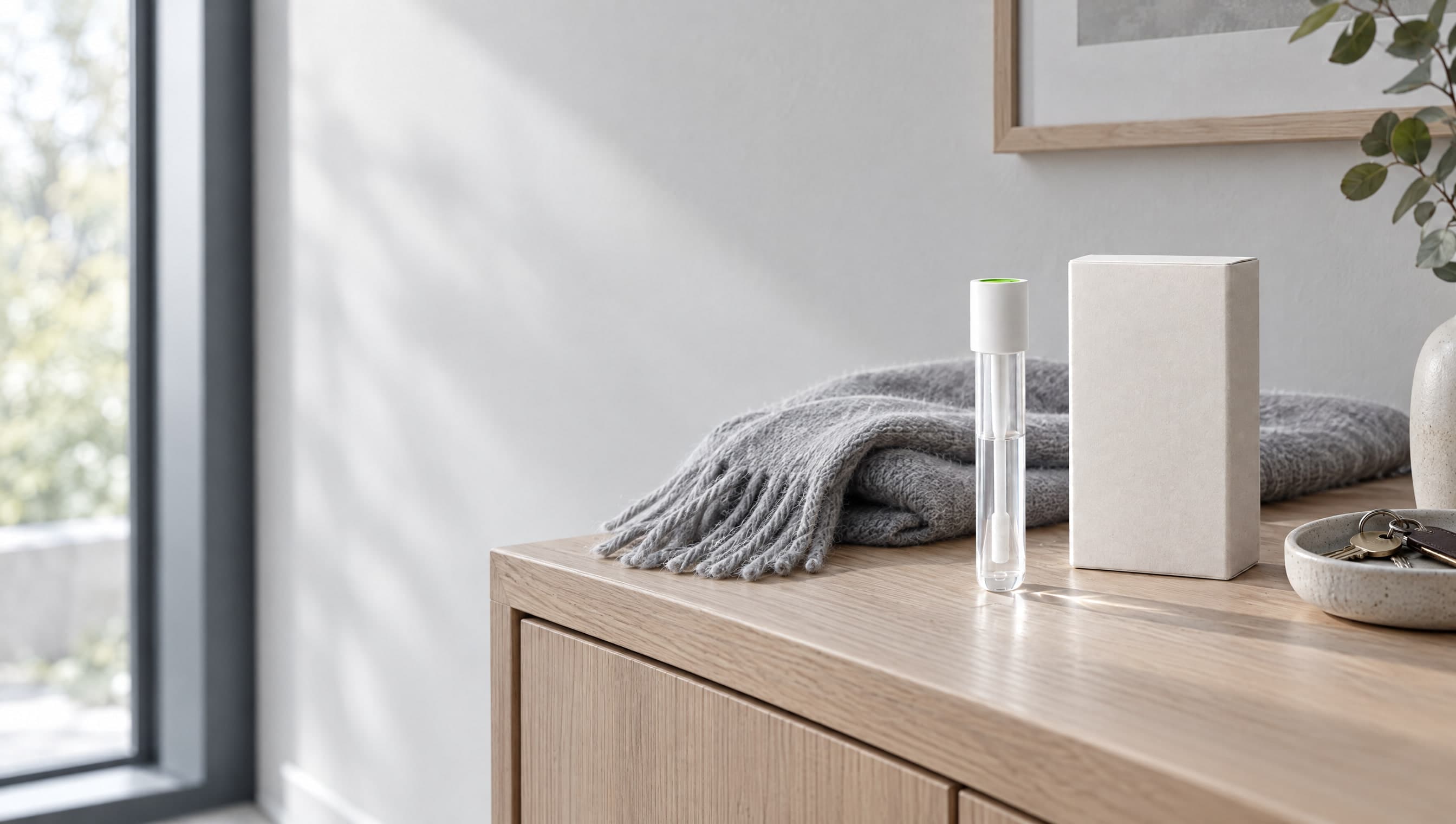 The GeneMatrix kit and its collection tube on an oak entryway console, beside a folded grey scarf and a key tray.