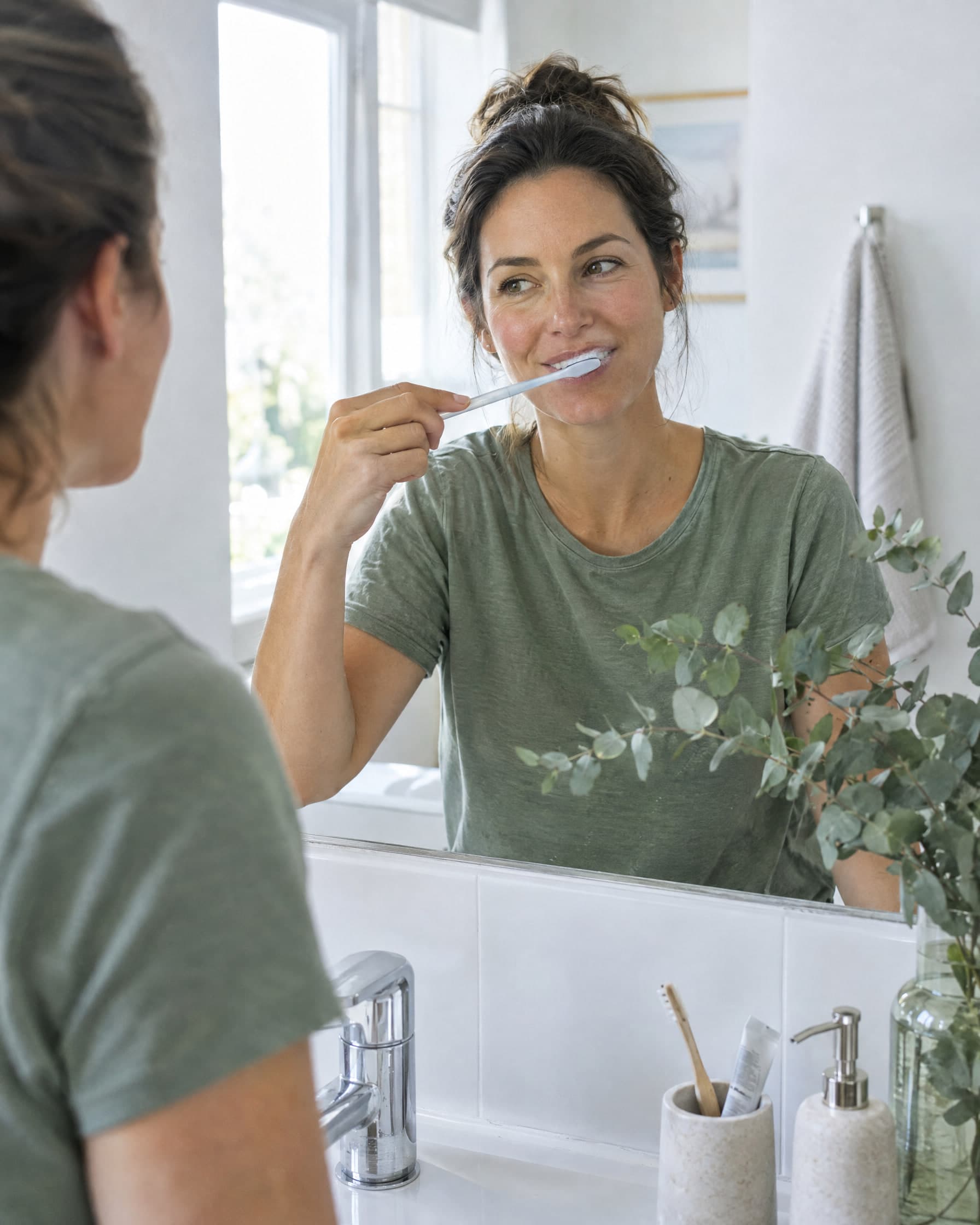 A woman brushing her teeth at a bathroom mirror in the morning.