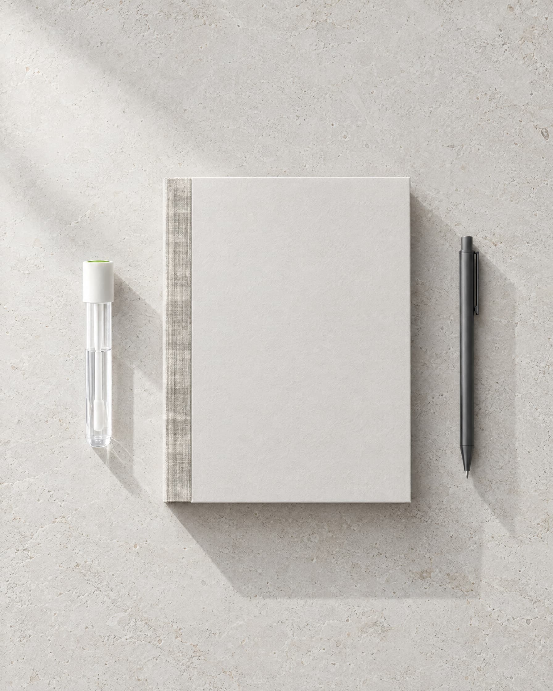 From above: the collection tube, a blank linen-bound report binder and a pen on pale stone.